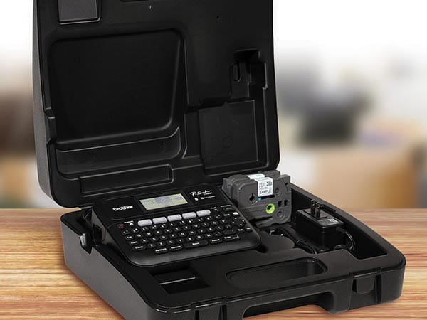 Label maker, 2 label tape cartridges, and AC adapter in carrying case on office desk