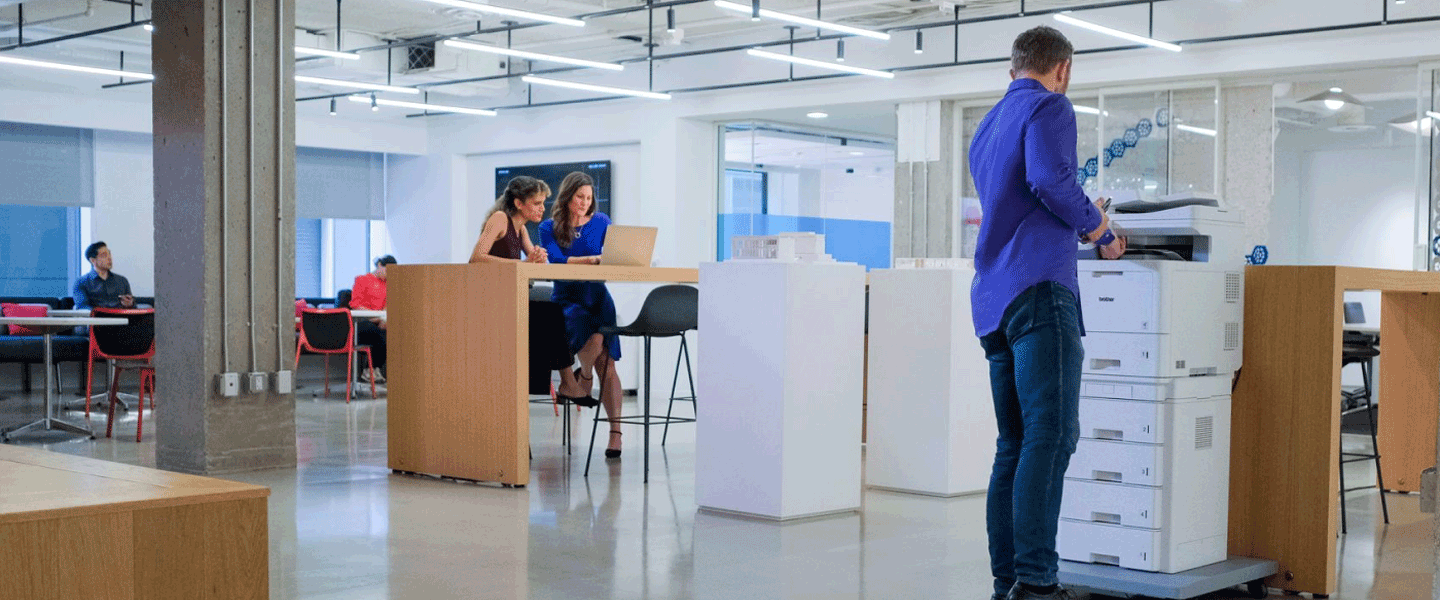 Office setting showing people collaborating and a person using a Brother enterprise all-in-one printer