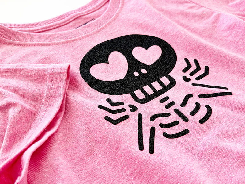 Shrugging skeleton applique on pink shirt with arm folded over