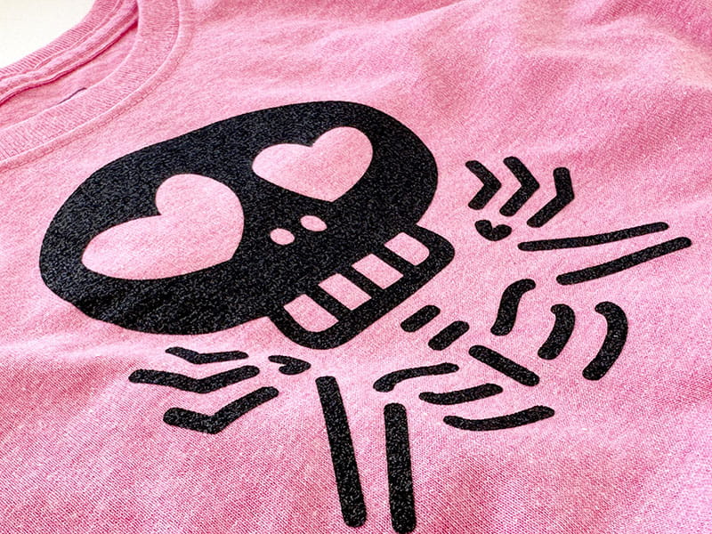 Close up of shrugging skeleton applique on pink shirt.