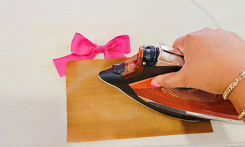 Person ironing right side of pink hair bow