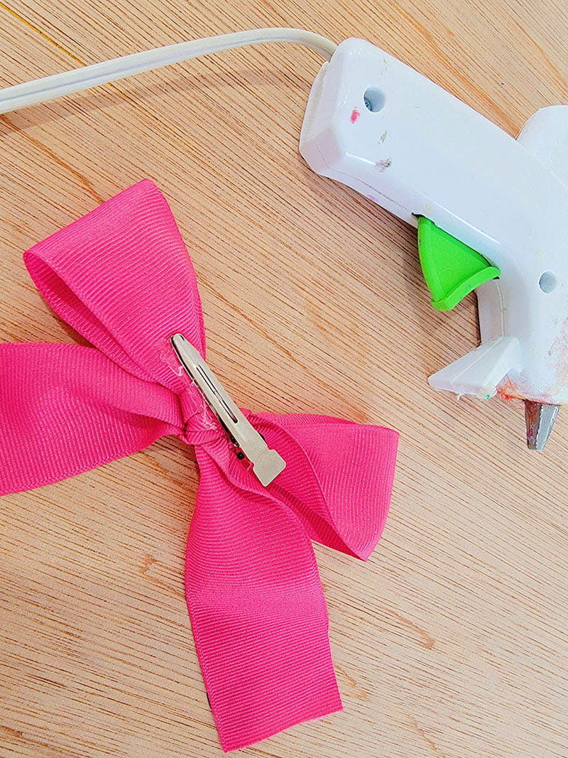 Back side of pink hair bow with alligator clip attached with a hot glue glue