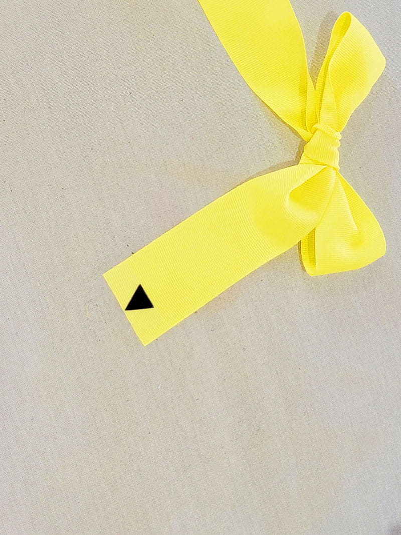 Yellow hair bow made to look like pencil with a black pointed tip on right side