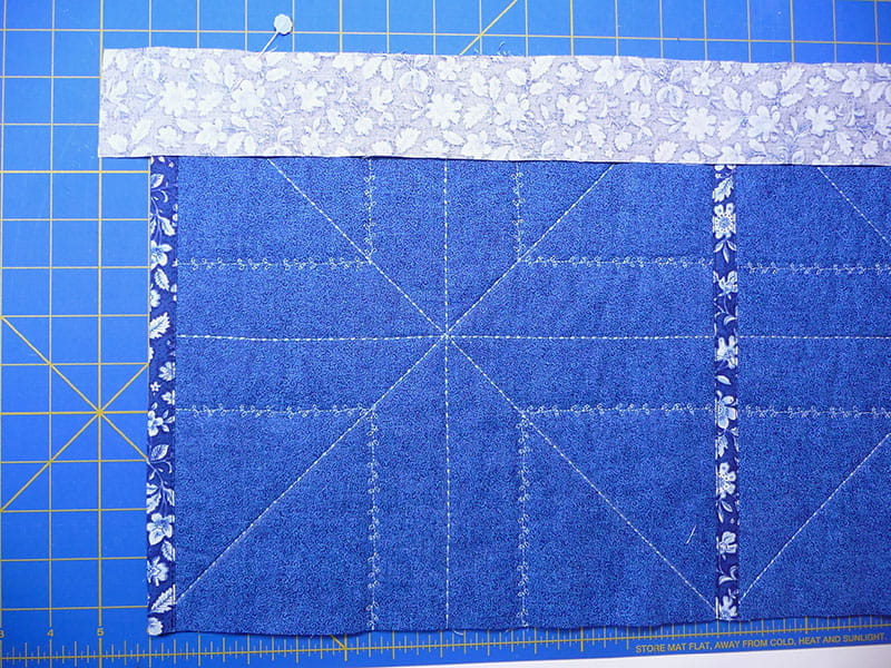 Top view of sewed fabric with pins on the top holding a corner piece in place