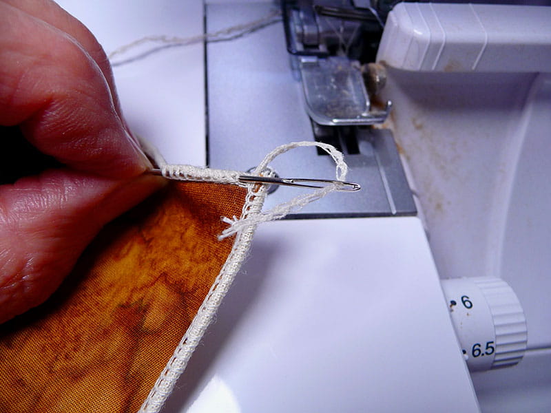 Person showing serge stitch on fall colored fabric next to serger machine
