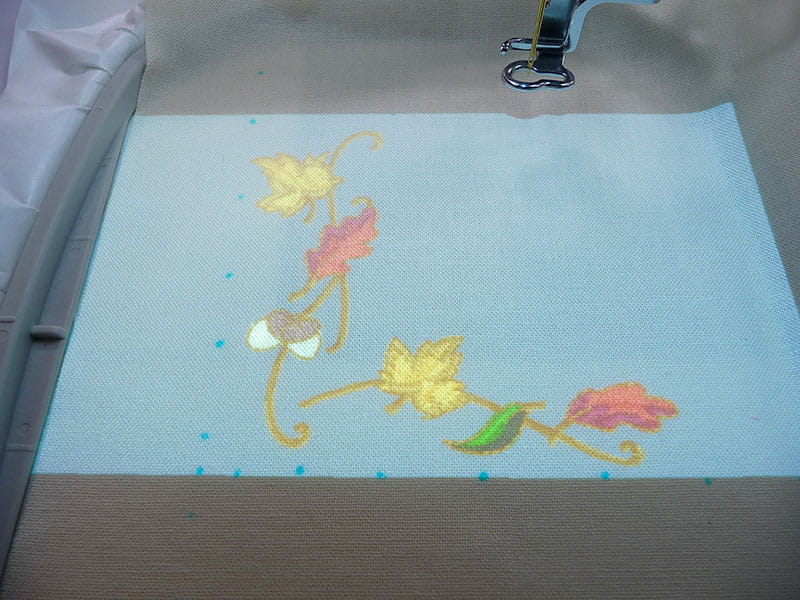 Light projecting from embroidery machine on leaf embroidery design on napkin. 