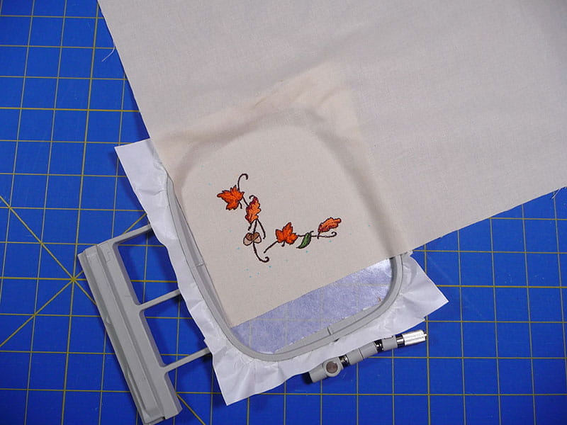 Completed leaf embroidery in embroidery hoop on a blue sewing board. 