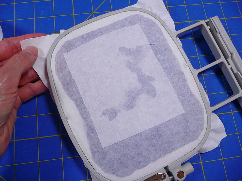 Backing of embroidery design in hoop on a blue sewing baoard