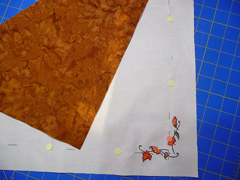 Napkin folded over showing orange marbled side and leaf embroidery on cream side. 