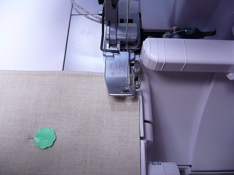 Napkin showing one side with serge stitch and set up to begin serge stitch on right side of fabric.