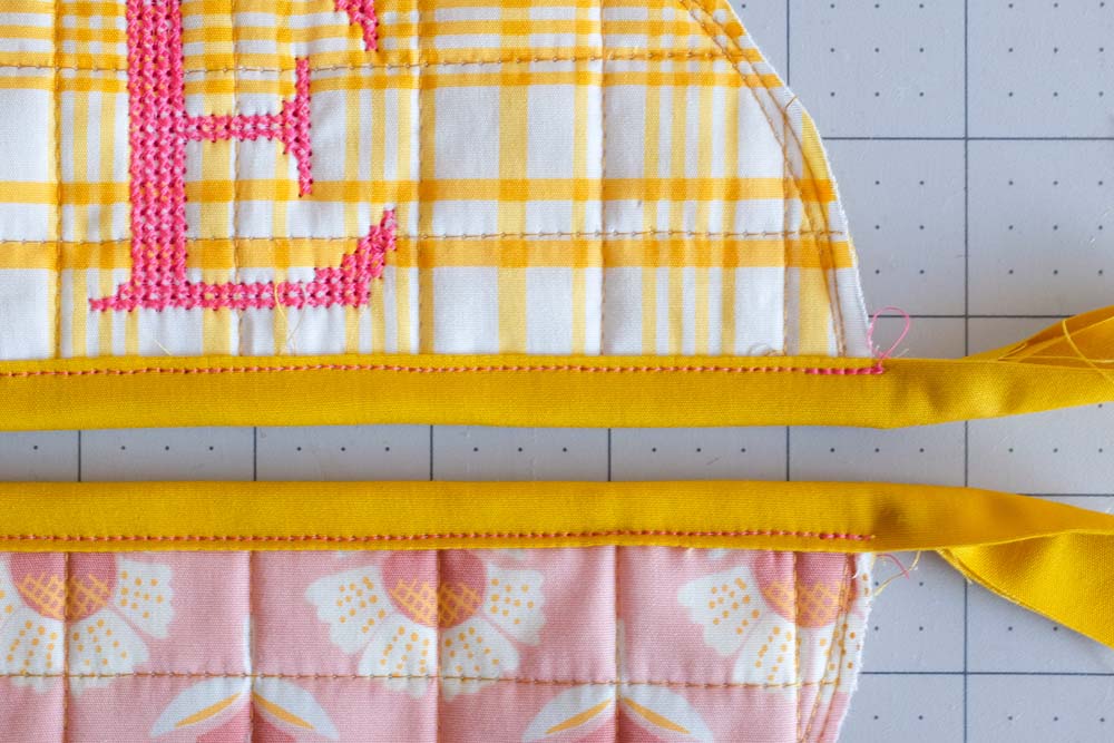A close-up of the yellow binding stitched onto the monogrammed yellow fabric and the pink floral fabric, highlighting neat stitching details.