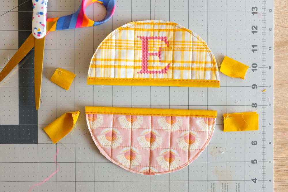 The two semicircles from the previous image are trimmed and arranged with colorful scissors and scrap fabric pieces nearby on the cutting mat.