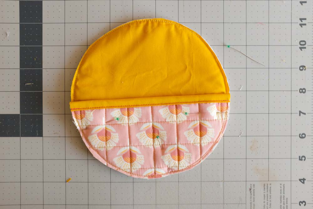 A full circular piece formed by combining a yellow quilted fabric backing and the pink floral semicircle on top, pinned and ready for assembly.