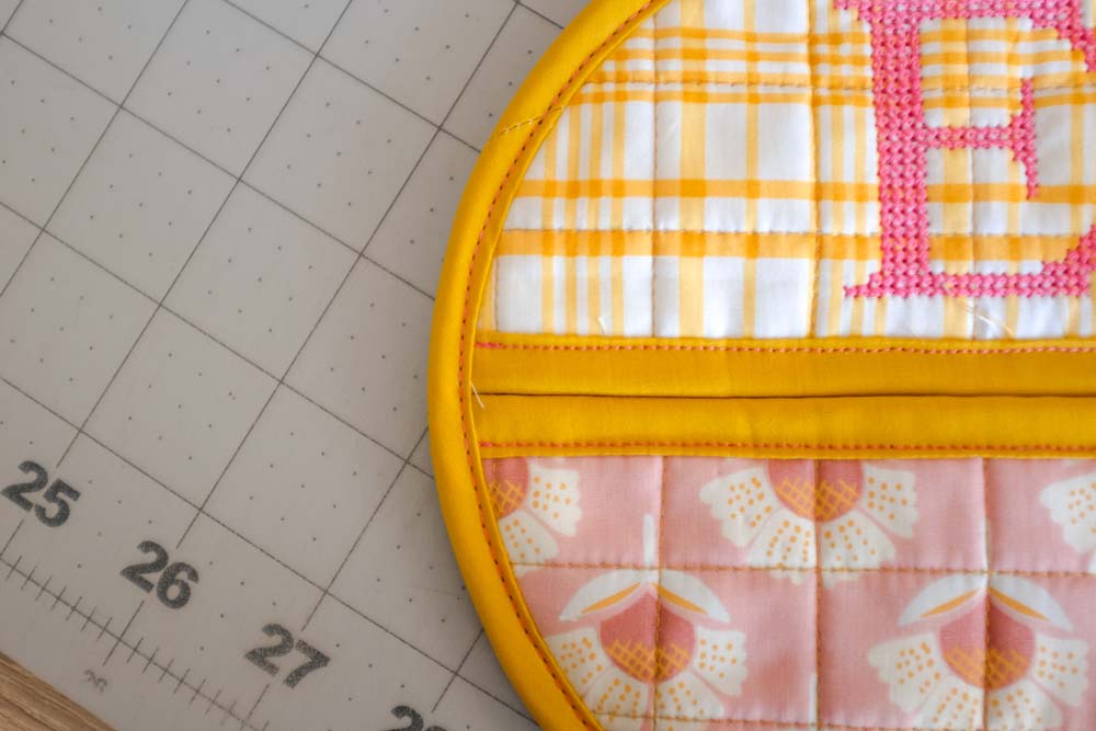 Close-up of the top portion of the potholder showing the neat stitching of the yellow binding against the yellow plaid fabric.