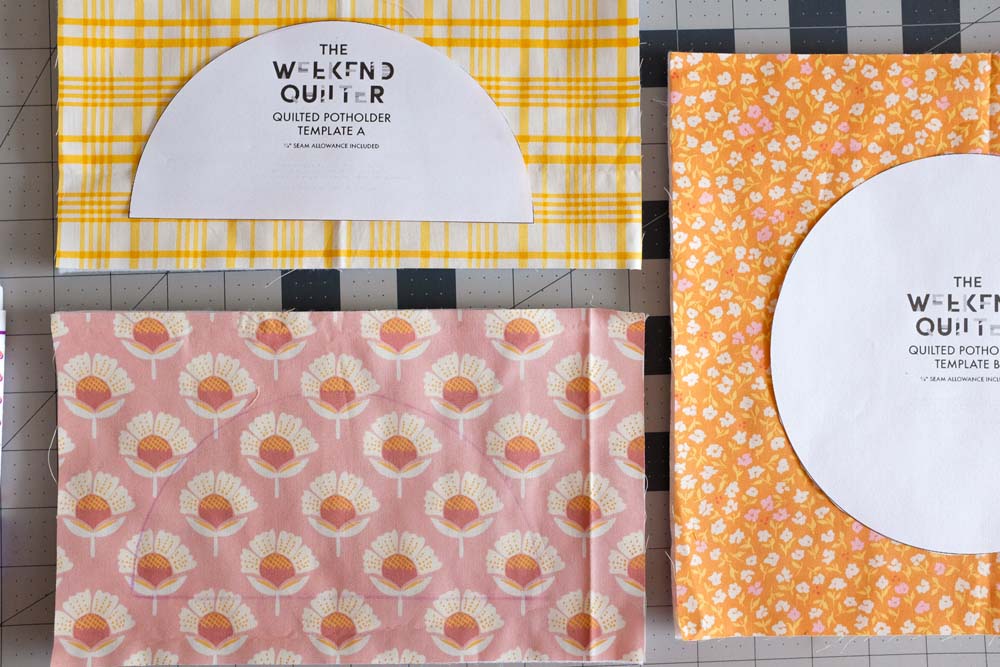 Fabric pieces with batting layers and semicircle templates labeled "The Weekend Quilter" placed on top. The fabrics include yellow plaid, pink floral, and orange floral patterns, laid neatly for cutting.