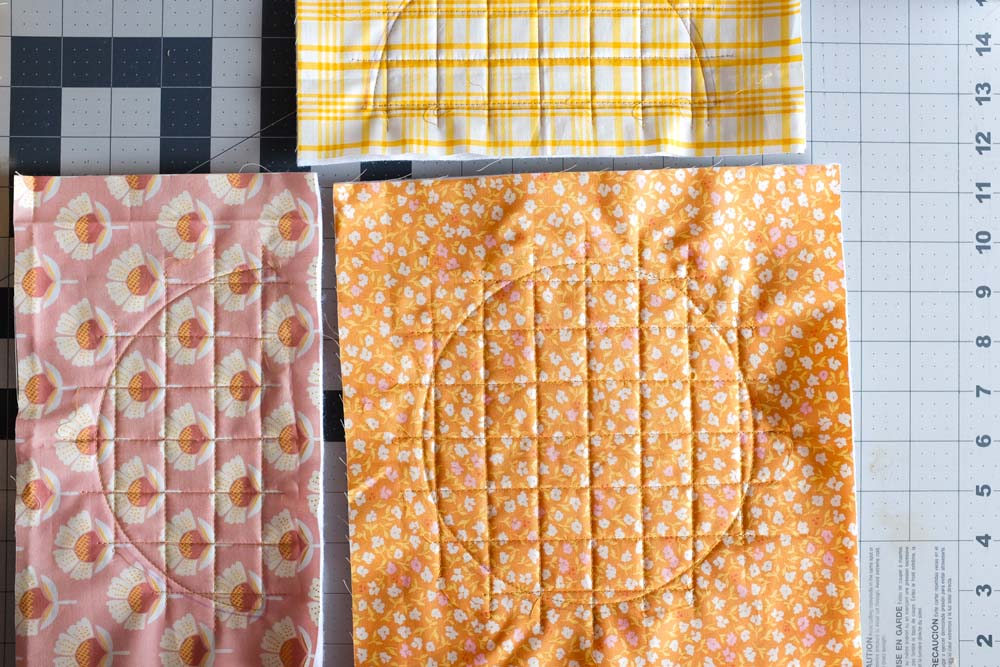 Three fabric panels featuring grid quilting, each with different patterns: yellow plaid, pink floral, and orange floral. Quilted lines form neat squares, and circle outlines are visible on the fabric.
