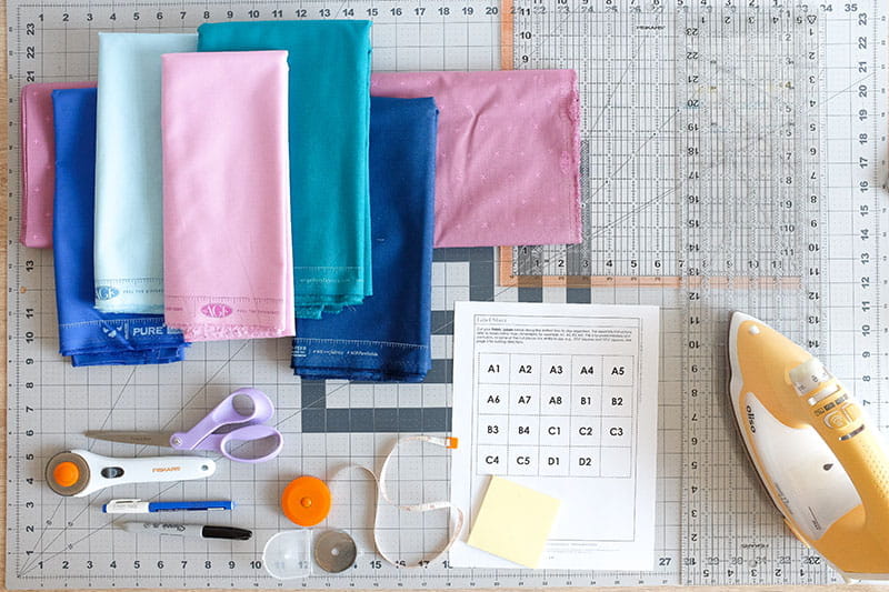 Fabric in various colors and quilting supplies on a cutting board. 