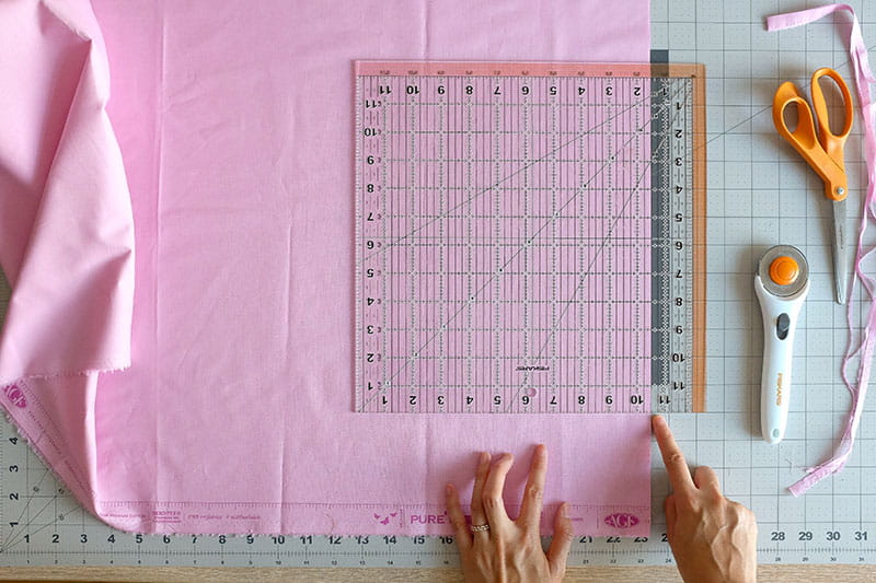 person measuring fabric square on cutting board
