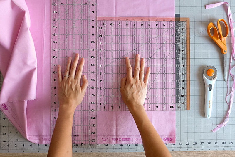 Person measuring pink fabric with 2 rulers 