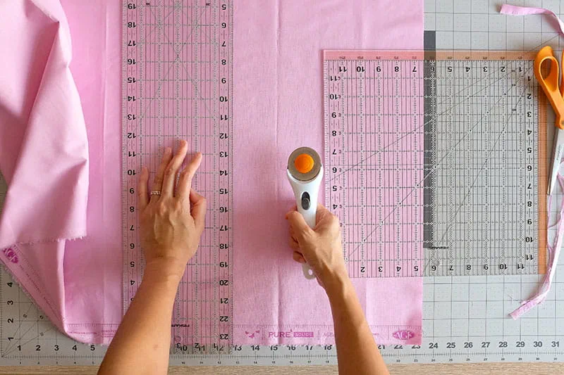 Person using rotary cutter to cut pink fabric on a cutting mat