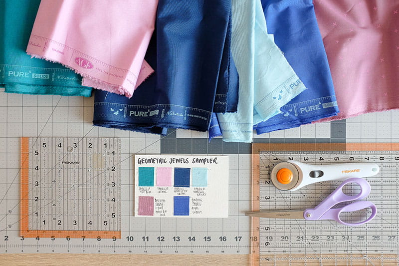 Various fabrics and quilting materials on a cutting board with rotary cutter and scissors