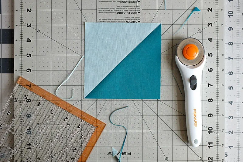 Teal and light blue fabric with trimmed edges next to a rotary cutter on cutting board.
