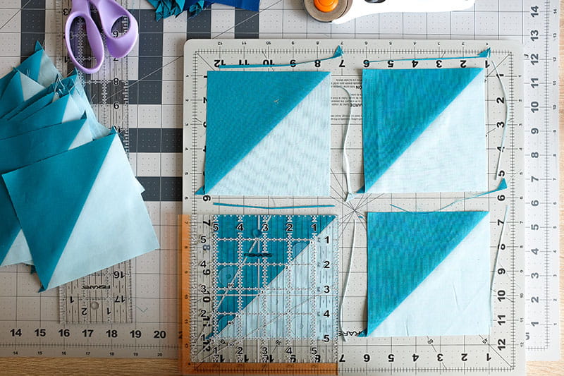 3 teal and light blue fabric squares with edges trimmed and one with straight edge overlaid for cutting