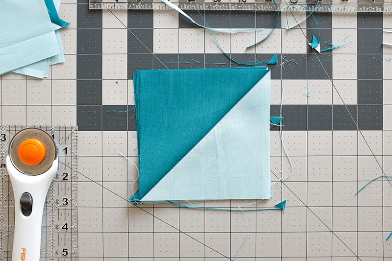 Half square triangle with fabric trimmings from rotary cutter on a cutting board.