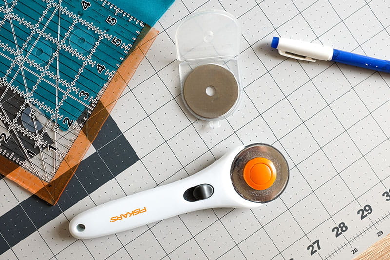 Quilting ruler, rotary cutter and fabric pen on a cutting board.