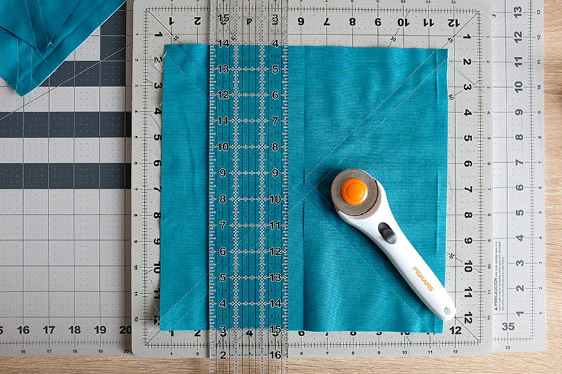 Large square of teal fabric on a cutting board with quilting ruler on top and fabric cutter.