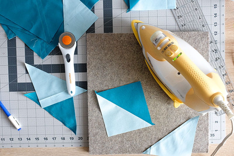 Iron next to two one half square triangle with additional fabric triangles to the side.