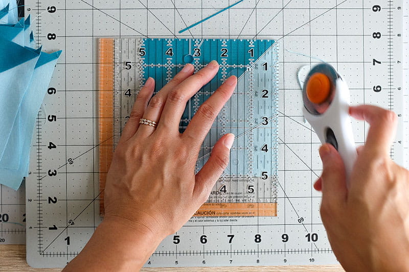 Person using rotary cutter and quilting ruler to create straight edge of half square triangle.