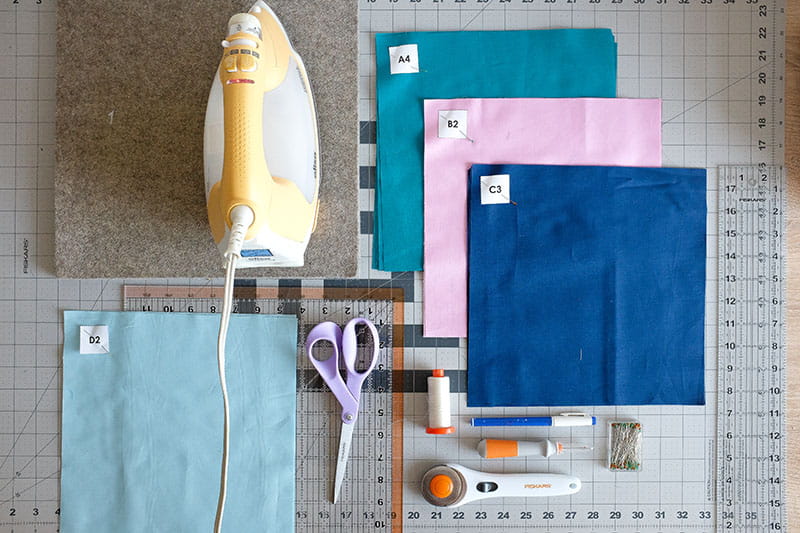 Quilting supplies including iron, fabric squares, scissors, rotary cutter and quilting rulers