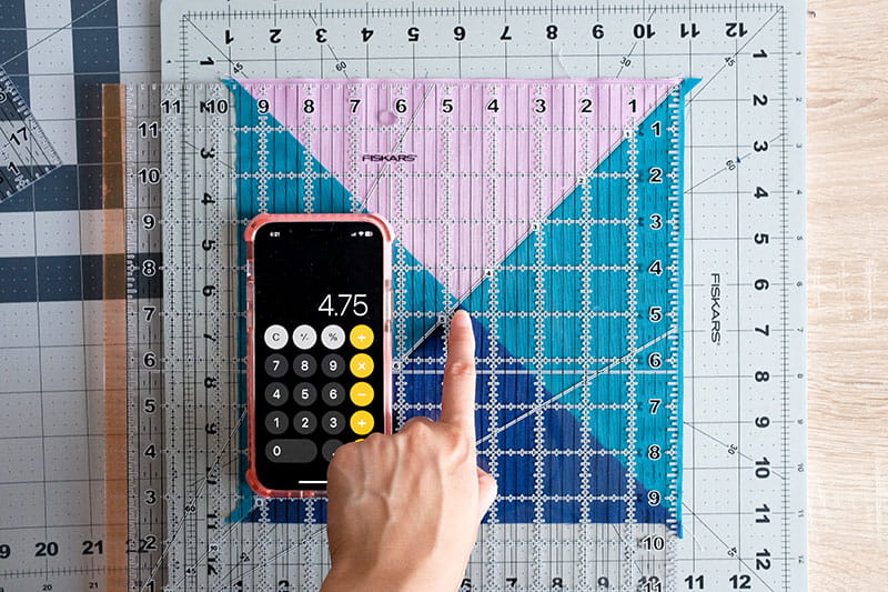 Person holding quilting ruler on top of fabric to find center point of the quarter square triangles.