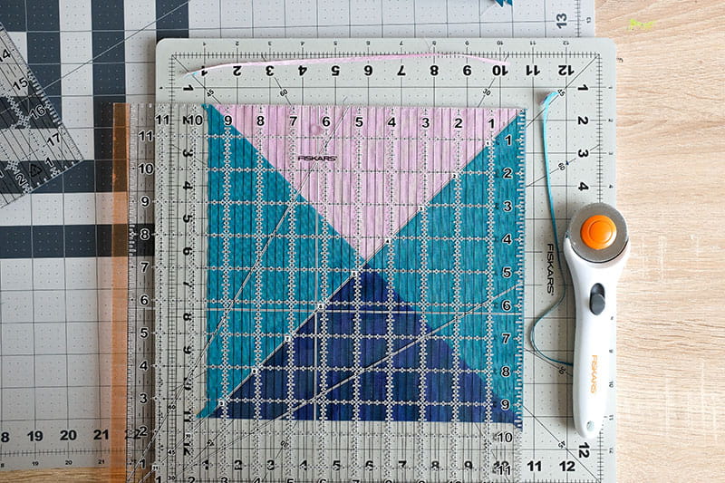 Quarter square triangle blocked fabric under a quilting ruler used to straight edge for rotary cutter