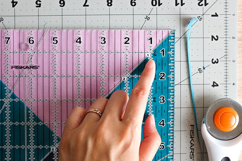 Close up of alignment for quarter square triangle with person pointing to the 45 degree angle on quilting ruler
