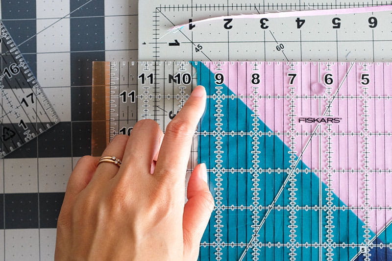 Person lining up the left side of quarter square triangle quilt pattern on a sewing board.