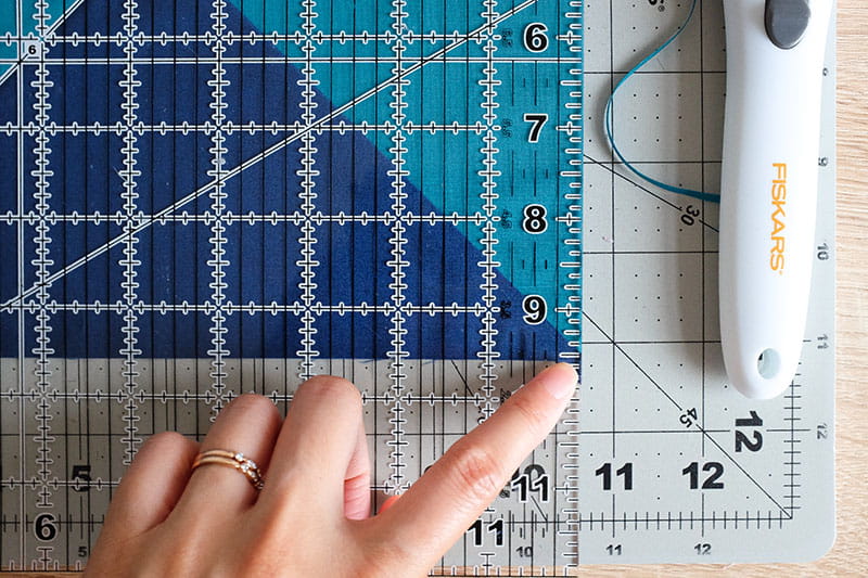Person lining up bottom right of quarter square triangle quilting fabric block on a cutting board.