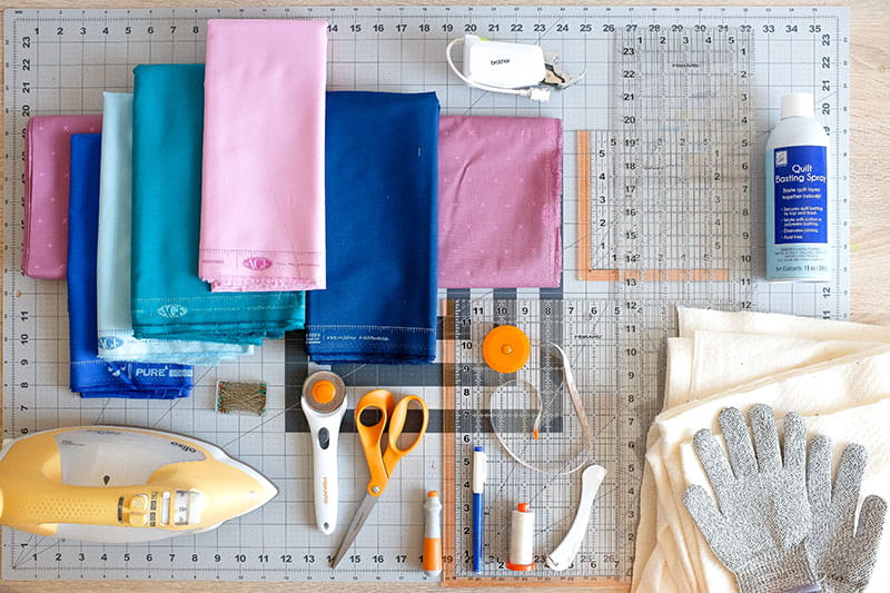 Quilting supplies on a sewing mat including an iron, fabric, scissors and circle cutter.