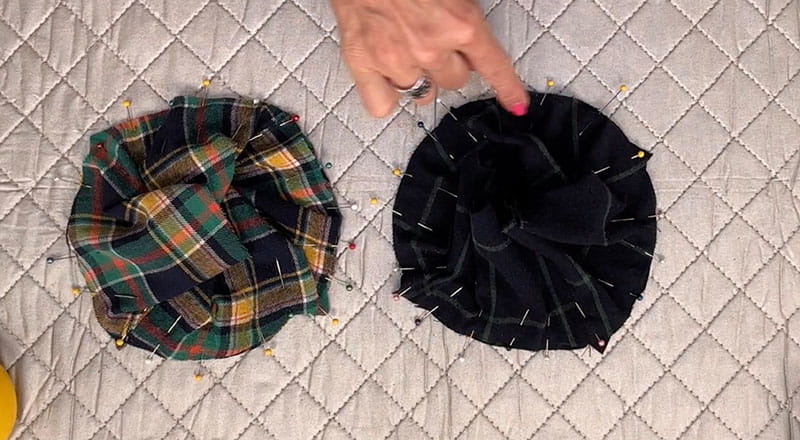 hand pointing at black cloth with pins, on the side is colorful cloth from a cut flannel shirt