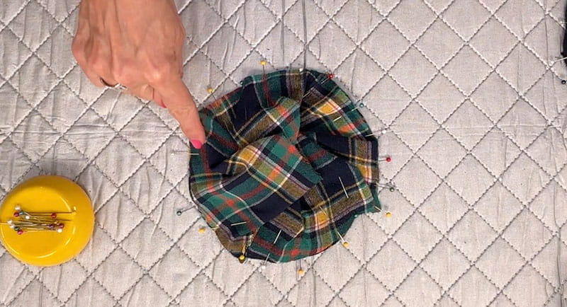 hand pointing at bucket hat cloth, white background, pins around the cloth