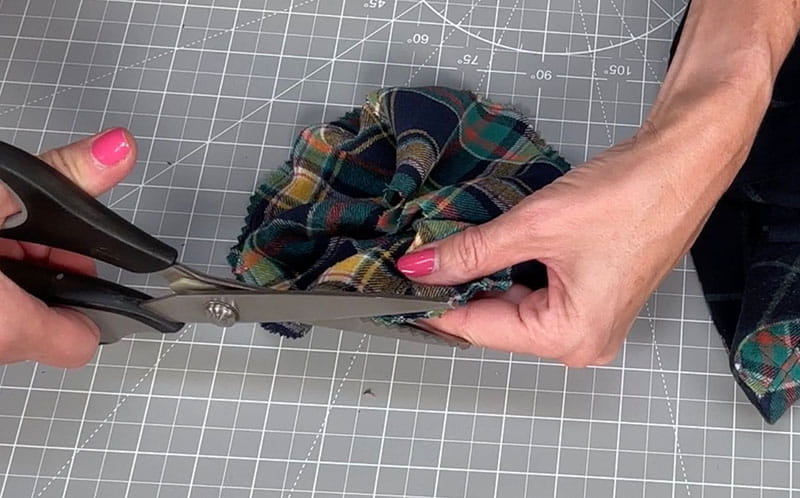 hand holding the cloth of the fabric while cutting it with black scissors