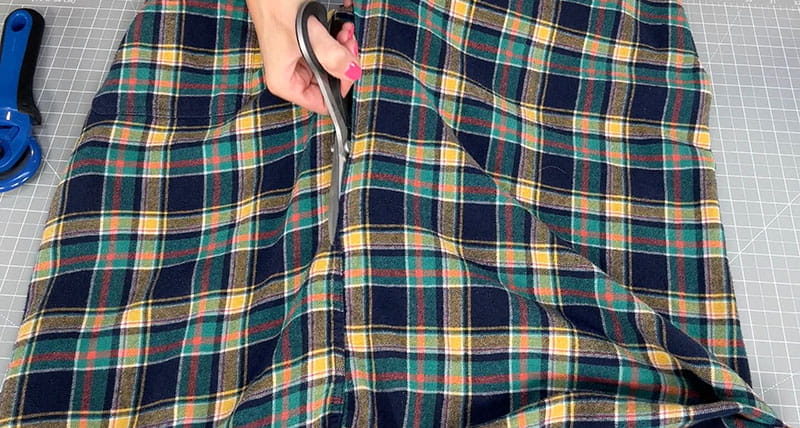 hand with scissors cutting through flannel shirt
