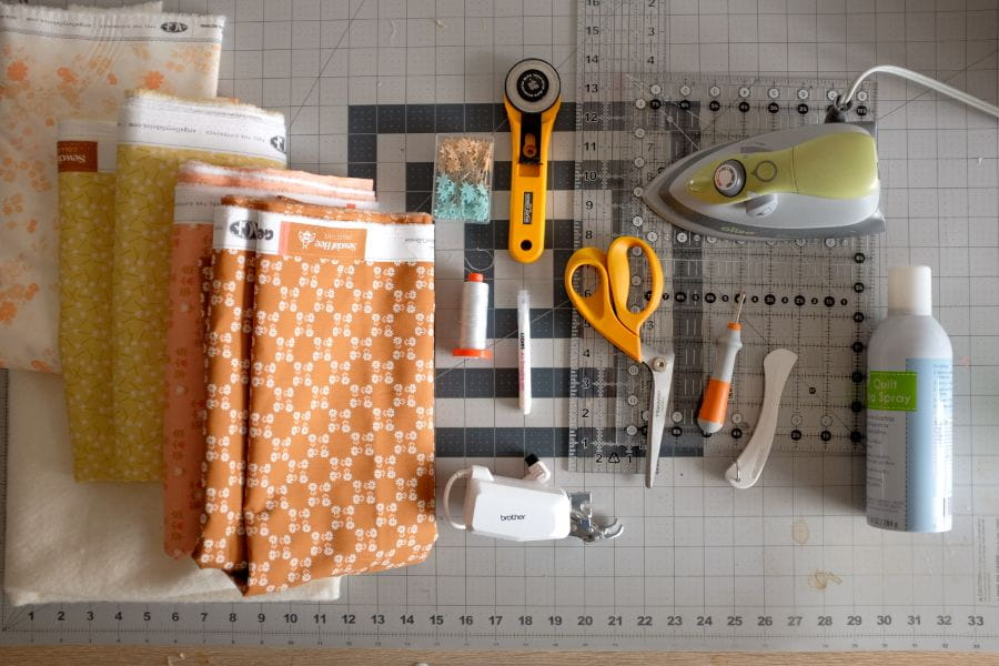 image of necessary quilting tools including scissors, rotary cutter, fabric, iron
