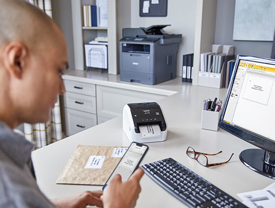 Man using phone and computer to create labels to print on the QL-1100 label printer