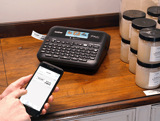 Person creating label on cell phone and printing on PT-D610BT label maker on a counter next to candles.