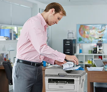 Man copying a document on MFC-L2759DW all-in-one in a small office. 