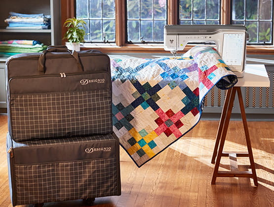 XJ2 luggage set next to a quilt in a craft room.  